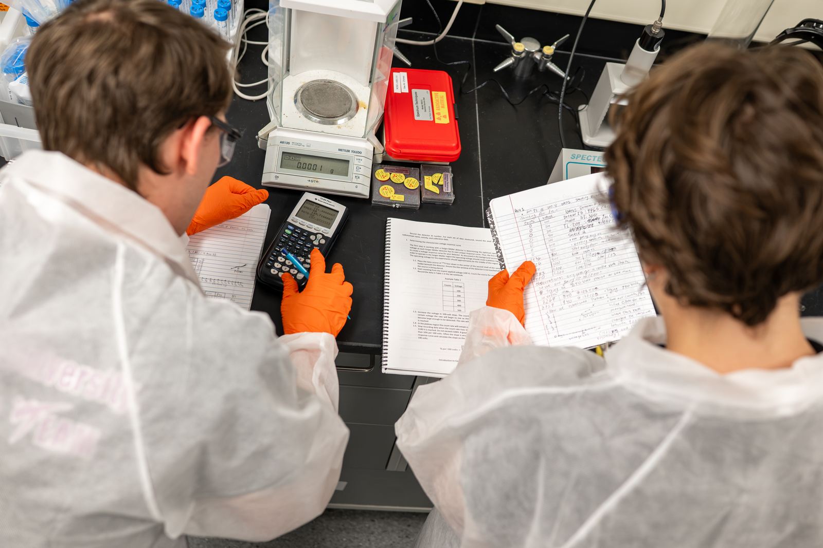 Two NCSS students weigh samples and take notes at a lab bench